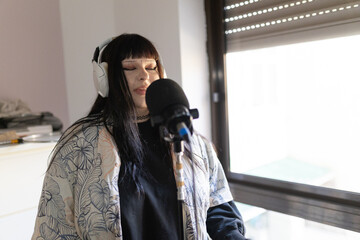 Young woman recording music, podcasting, or singing at home