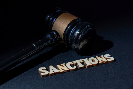 A wooden gavel next to the word SANCTIONS on a dark background. International law, legal penalties, trade restrictions, economic policy, and corporate punishment concept. - Powered by Adobe