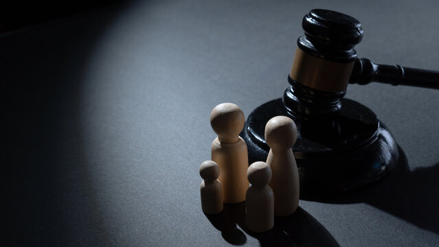 A wooden gavel next to a group of four wooden peg dolls. Family law, legal justice, child custody, social policy, and family protection concept.