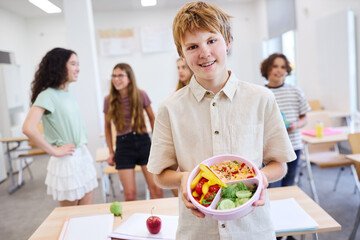 Smiling student holding healthy meal in a classroom environment