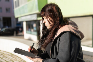 Young woman writing notes in a planner outdoors