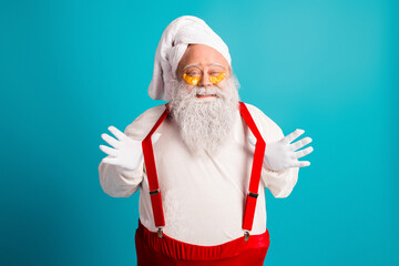 Santa in red suspenders and white outfit with a towel on his head and yellow eye masks poses playfully for a festive holiday scene against a blue background