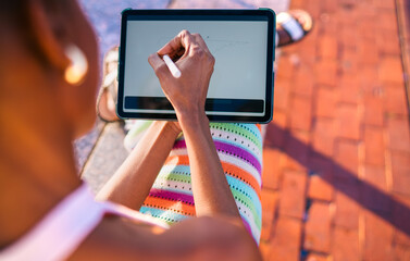 Overhead view of African woman drawing on tablet with digital pen, blending creativity, technology, and colorful personal style in urban outdoor workspace.