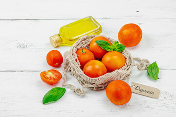 Fresh home-grown tomatoes, basil leaves and olive oil on a white wooden surface. Organic ingredients