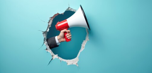 Hand in suit breaks through blue wall holding red white megaphone. Making announcement, calling attention, or shouting news. Promoting services, searching candidates, or sharing info.