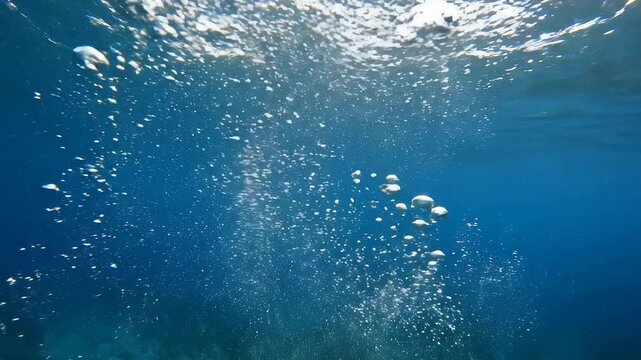 Air bubbles ascend rapidly deep in clear blue ocean water