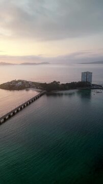 Aerial view of Toralla island connected by a bridge, where a modern building stands against the backdrop of the sunrise, illa de Toralla, Pontevedra, Spain.