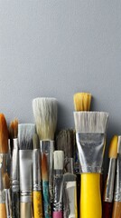 Fototapeta premium Collection of used artist paint brushes with varied bristles stands against textured grey background.