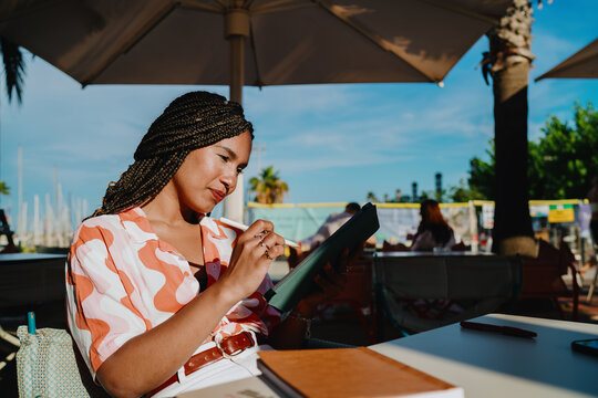 Young woman with braided hair using digital tablet and stylus outdoors, focused on creative work, symbolizing productivity, independence, and modern freelance lifestyle powered by technology.