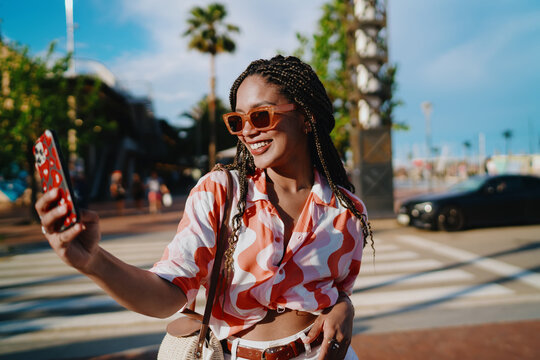 Confident young woman smiling while holding smartphone outdoors, symbolizing freedom, positivity, and empowerment through digital lifestyle and urban freelance culture. - Powered by Adobe