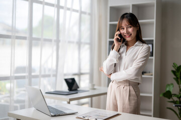 Asian businesswoman talking on phone, standing at desk in modern office