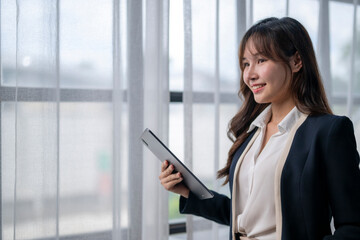 Smiling businesswoman holding tablet and looking through office window