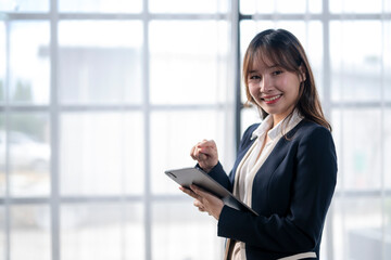 Obraz premium Smiling businesswoman using digital tablet in modern office by window