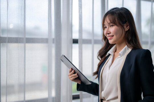 Smiling businesswoman holding tablet and looking through office window