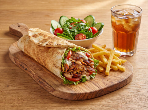 Delicious Chicken Shawarma Wrap Served with French Fries, Fresh Green Salad, and Iced Tea on Wooden Board