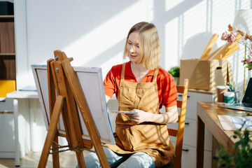 A female artist painting on canvas in a bright home studio, expressing creativity and focus.