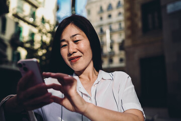 Joyful midlife woman uses smartphone with bright smile, representing digital happiness, social interaction, and effortless tech integration into everyday urban lifestyle.