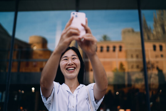 Smiling woman takes selfie with smartphone, surrounded by historic architecture, blending heritage, emotion and contemporary digital habits.