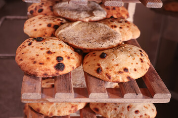 Freshly baked traditional flatbreads displayed on wooden shelves in a bakery, showcasing rustic texture and golden crust perfect for food markets and culinary themes.