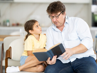 Fototapeta premium Father reads book to little cute daughter, spend leisure enjoy good life hobby and pastime at home. Fatherhood, upbringing, children development