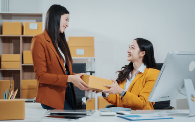 Asian female entrepreneurs coordinating product handover at an e-commerce office, preparing parcels for shipping logistics while collaborating professionally to manage online business operations