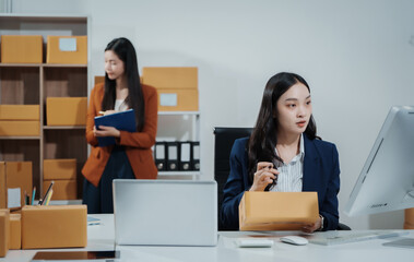 Asian female entrepreneurs coordinating product handover at an e-commerce office, preparing parcels for shipping logistics while collaborating professionally to manage online business operations