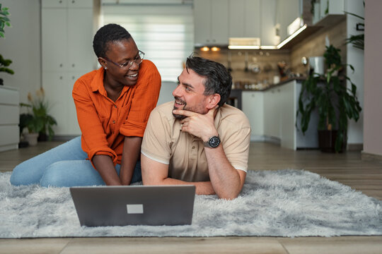 Happy multi-ethnic couple relaxing on the floor using laptop at home