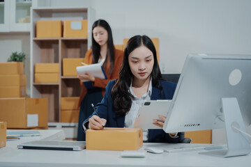 Asian female entrepreneurs coordinating product handover at an e-commerce office, preparing parcels for shipping logistics while collaborating professionally to manage online business operations