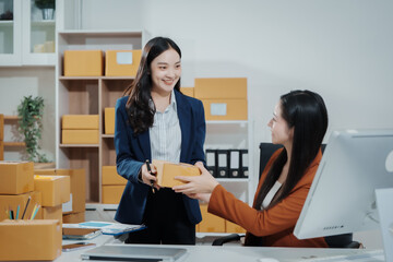 Asian female entrepreneurs coordinating product handover at an e-commerce office, preparing parcels for shipping logistics while collaborating professionally to manage online business operations