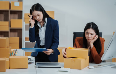 Two young Asian business woman stressed over poor sales, struggling with e-commerce order management, inventory, and logistics issues, showing visible frustration and pressure while handling parcels