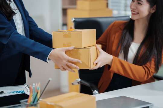 Asian female entrepreneurs coordinating product handover at an e-commerce office, preparing parcels for shipping logistics while collaborating professionally to manage online business operations