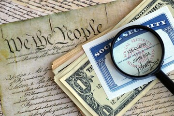 SSN Social Security Number card Under magnifying glass with dollar bills on US Constitution close up