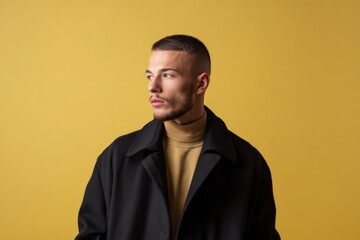 Obraz premium Young caucasian male in black coat on yellow background looking away thoughtfully