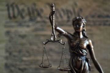 Lady Justice and background of US Constitution page close up. Lawsuit and judgement in United States of America