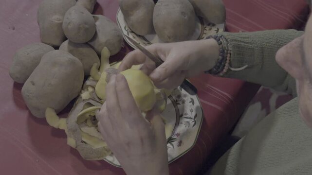 Woman's hands peeling raw potatoes with a knife