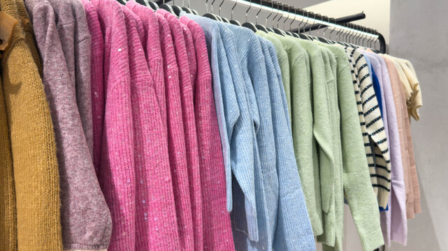 Soft colorful sweaters in pink, blue, green and pastel tones neatly hanging on a rack inside a bright clothing store, creating a cozy and stylish winter display - Powered by Adobe