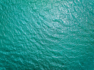 Top view of blue turquoise water surface texture with ripples and waves in sunlight.