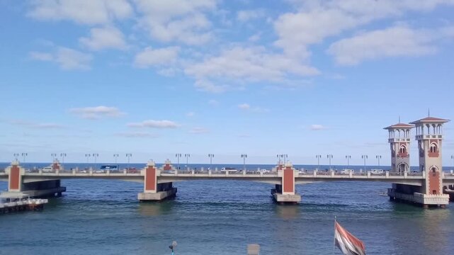 This is a great view of the Mediterranean Sea under Stanley Bridge. Some cars are running on the bridge. The bridge is on the Corniche Road in Alexandria, Egypt. It has a pedestrian walkway.