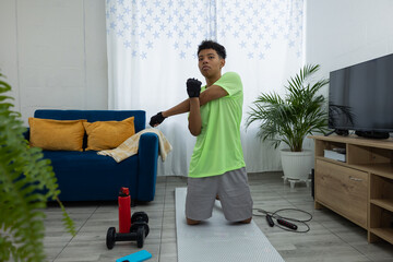 Latino teenager kneeling on a mat doing a hand stretch during his home workout routine, maintaining a healthy physical practice
