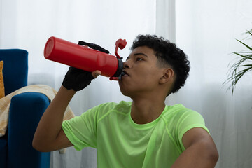 Close up of a Latino teenager hydrating with a red bottle during his home routine, representing an active and healthy lifestyle