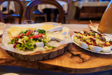 An artisanal wooden board holds soft ripened cheese with greens and tomato, with crostini topped with melted cheese, bacon, and herbs at a cozy bistro during evening.