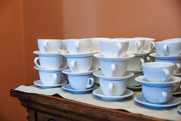 White porcelain teacups and saucers stack in neat towers on a wooden sideboard with a cream runner, handles aligned, warm indoor lighting, shallow depth of field.