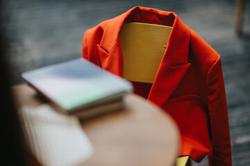 A bright red blazer rests on a mannequin bust beside a wooden table, with blurred books in the...