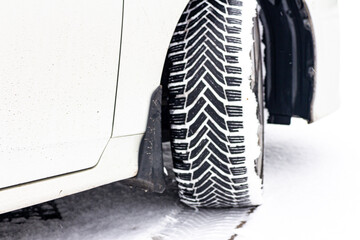 Close up of a car wheel with winter tire tread on snowy ground, showing detailed pattern © Alex Malt