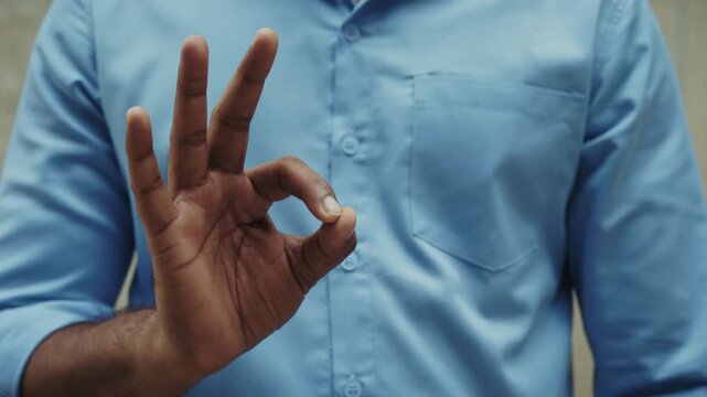 Crop view of Indian man shows Ok gesture while stands on grey background. Confident businessman expresses appreciation by hand sign closeup. Circle of thumb and index finger