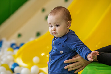 Cute baby at indoor playground slide with parent