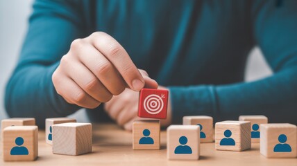 Strategic Goal Selection: A hand delicately places a cube marked with a target symbol atop blocks representing individuals, symbolizing strategic focus and team-oriented goals.