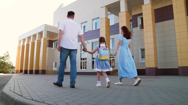 mother father leading child school holding hands, happy family, father mother holding child hands, family holding hand against backdrop school building, father mother escorting child school backpack - Powered by Adobe