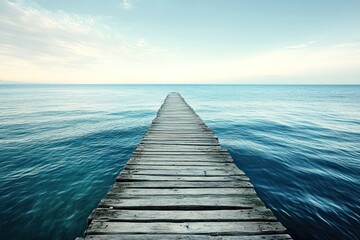 Obraz premium A wooden pier extends into the calm blue waters of the ocean, leading to a distant island. The sky is a clear blue, and the sun shines brightly, casting a warm glow on the scene.