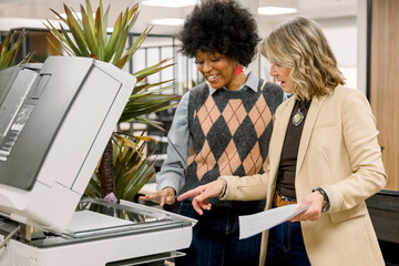 Diverse businesswomen using office photocopier collaborating at work